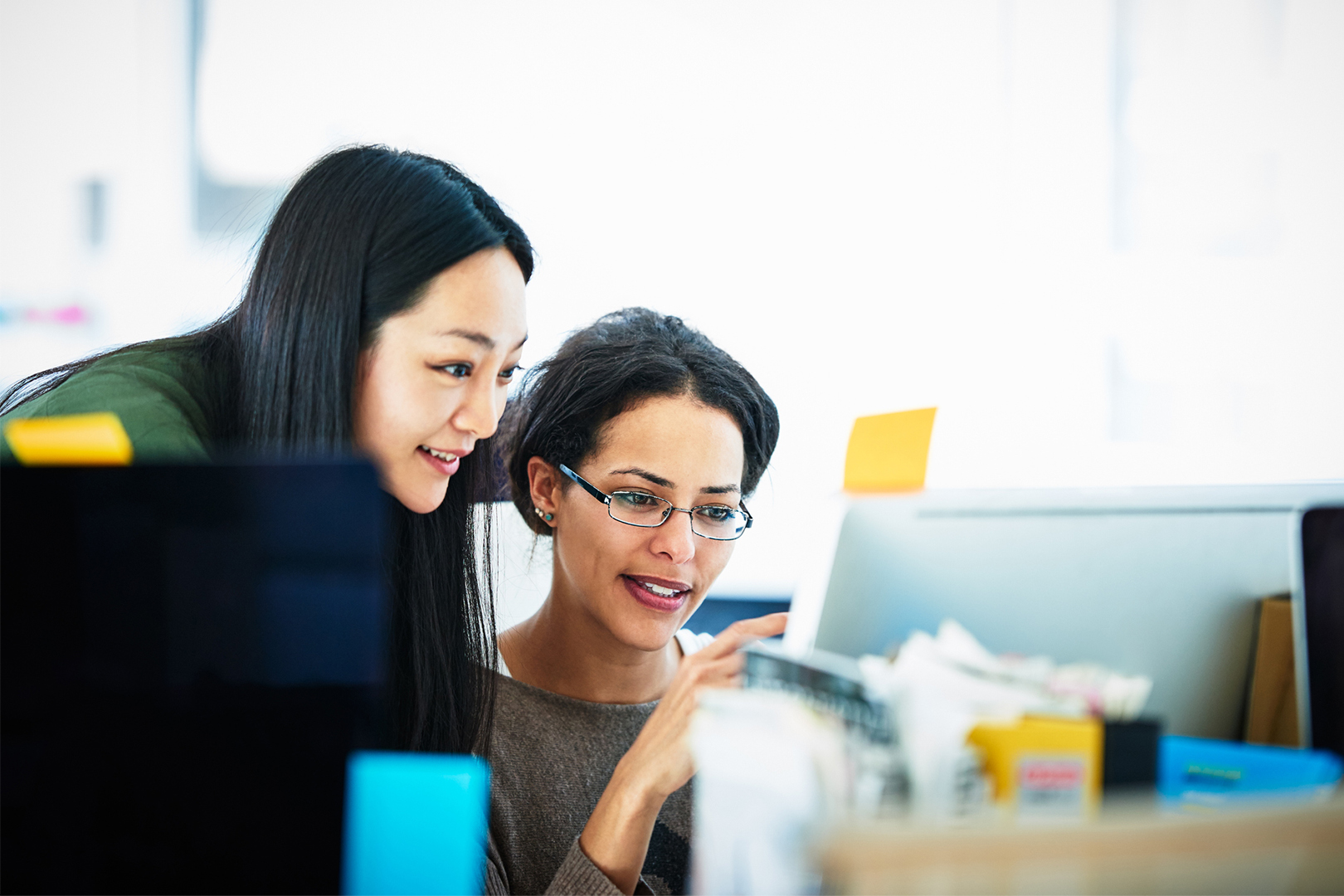 Two women looking behind a computer screen