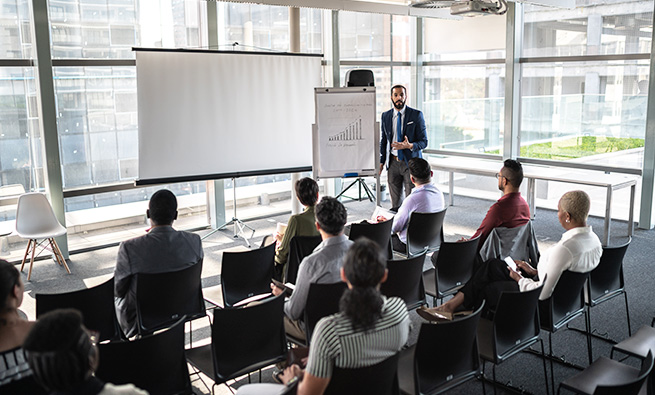 a man presenting on a whiteboard to a team